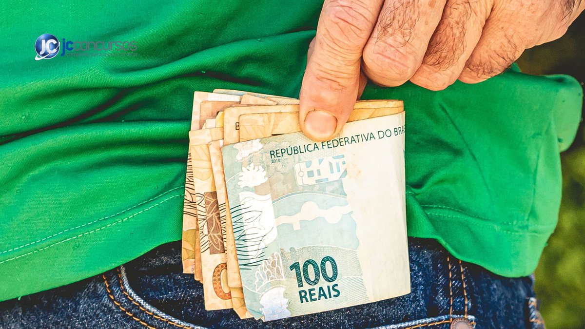 Um homem segura notas de dinheiro - Canva - Salário extra de R$ 1.302