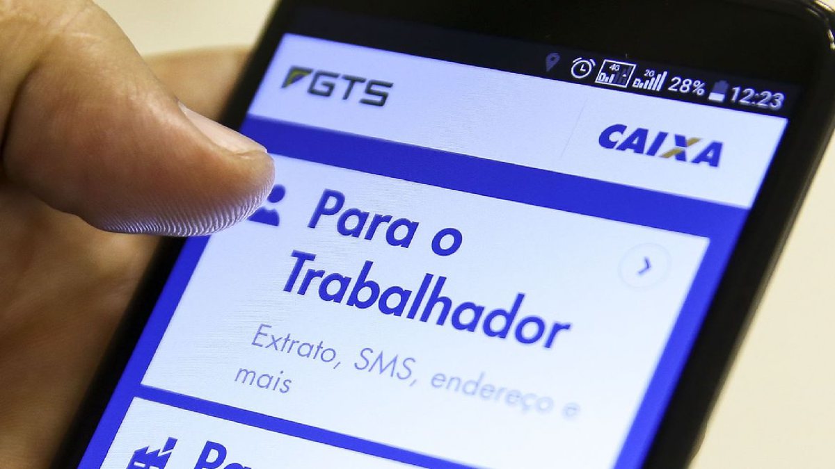 Um homem segura um celular aberto com o site do FGTS - Agência Brasil - Saque-aniversário do FGTS