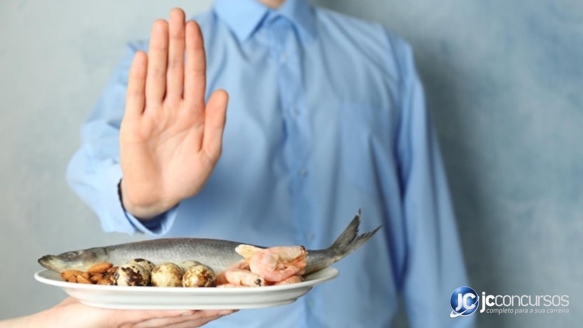 Pessoa com a mão em sinal de "não" ou "pare" para pratos com alimentos - Freepik