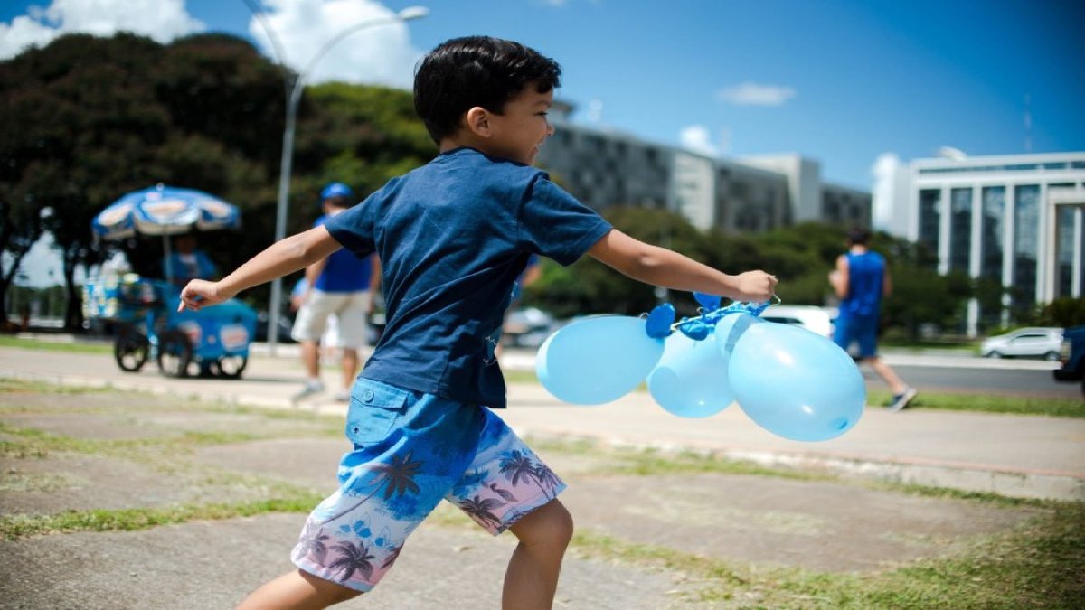 Criança com autismo corre e brinca com bexigas azuis
