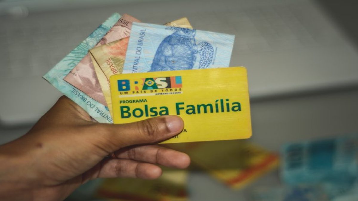 Uma mulher segura o cartão do Bolsa Família e notas de dinheiro
