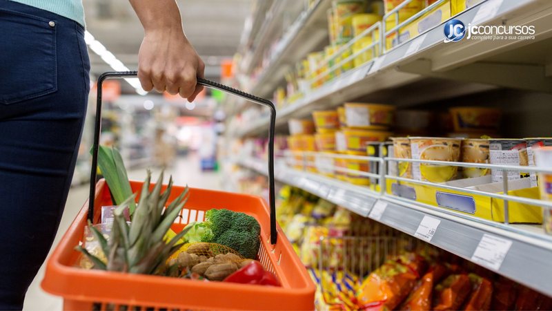 Mulher carrega cesta com alimentos em supermercado