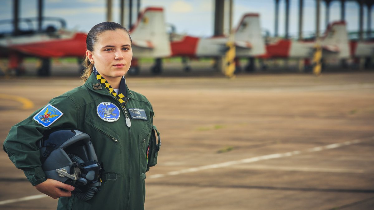 Concurso Aeronáutica: aviadora da Força Aérea Brasileira posa para foto com aeronaves ao fundo