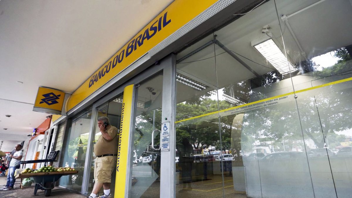 Concurso Banco do Brasil: homem passa pela porta de agência do BB falando ao celular