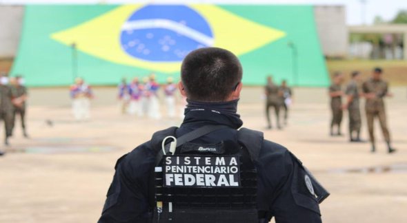 Concurso Depen: com bandeira do Brasil ao fundo, agente de segurança aparece de costas observando militares - Divulgação