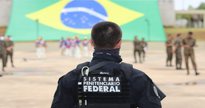 Concurso Depen: com bandeira do Brasil ao fundo, agente de segurança aparece de costas observando militares - Divulgação