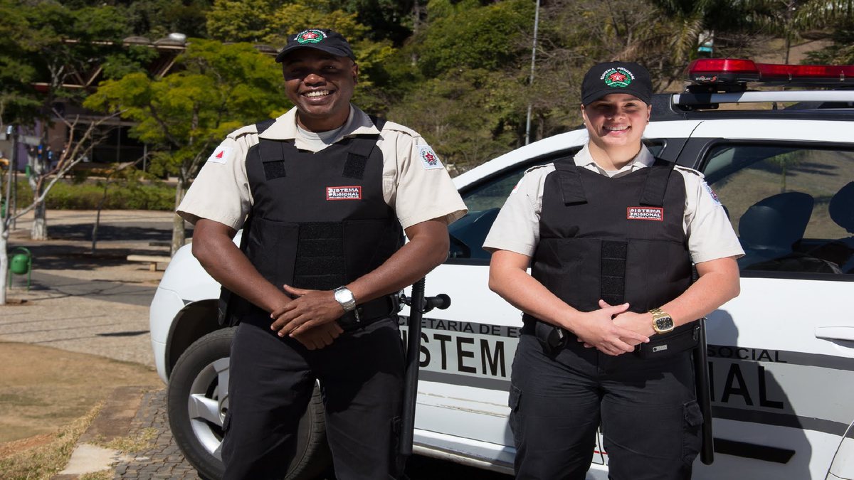 Concurso Depen MG: dois policiais penais posam para foto ao lado de viatura