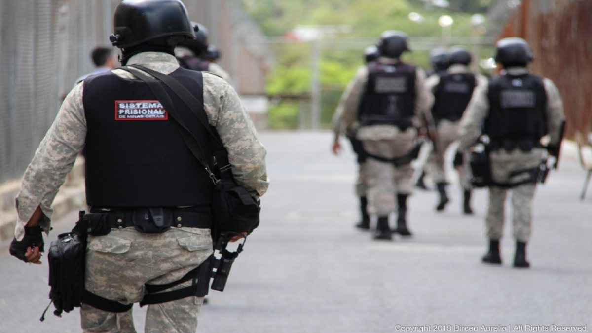 Concurso Depen MG: policiais penais aparecem de costas caminhando em unidade prisional