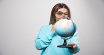 Mulher usa lupa para observar globo terrestre - Freepik/@azerbaijan_stockers