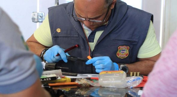 Concurso da Polícia Científica de Alagoas: perito utiliza lupa para examinar arma de fogo apreendida - Divulgação