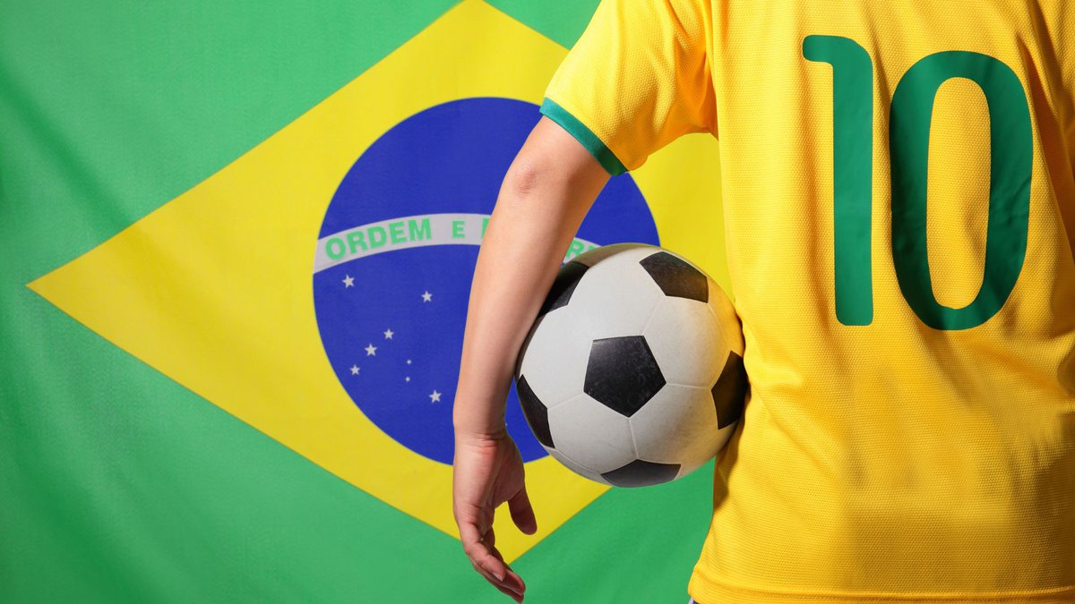 Jogador segura bola e bandeira do Brasil ao fundo