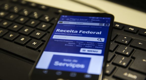 Um celular aberto com o site da Receita Federal embaixo de um teclado - Agência Brasil - Restituição do Imposto de Renda 2022