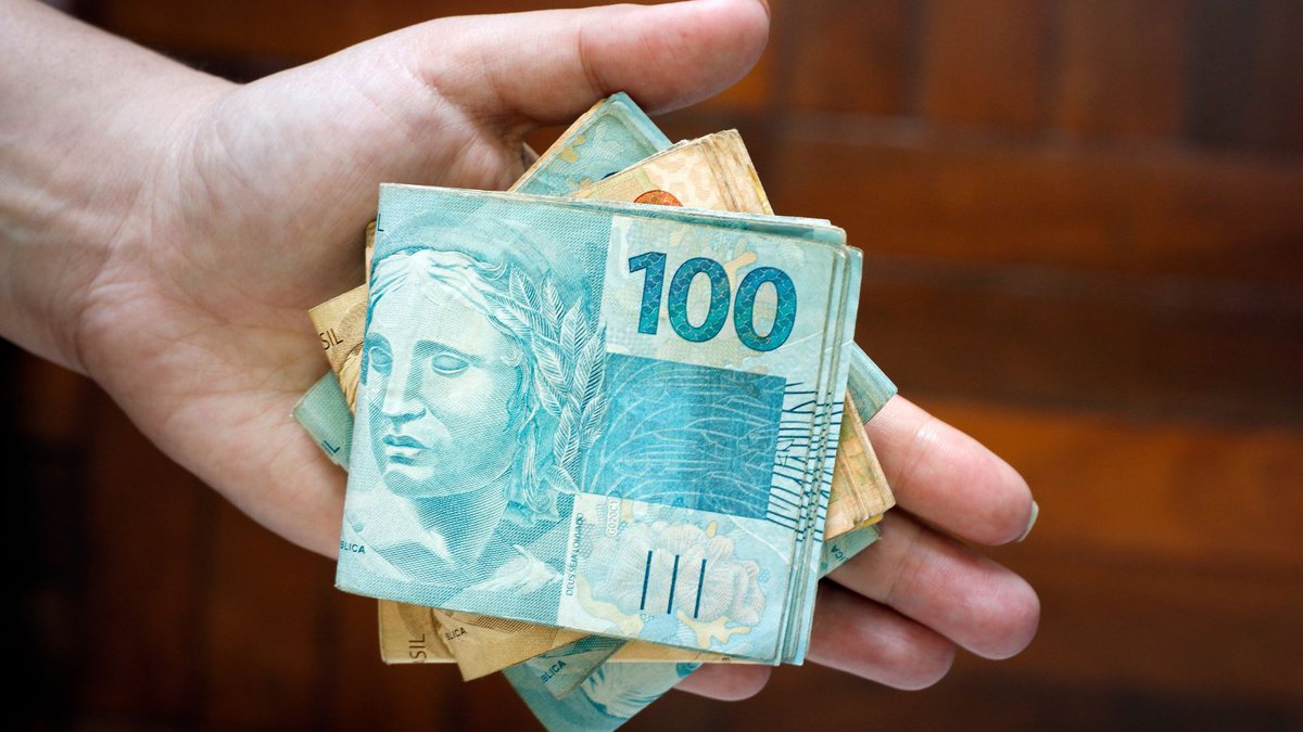 Um homem segura notas de R$ 100 e R$ 50