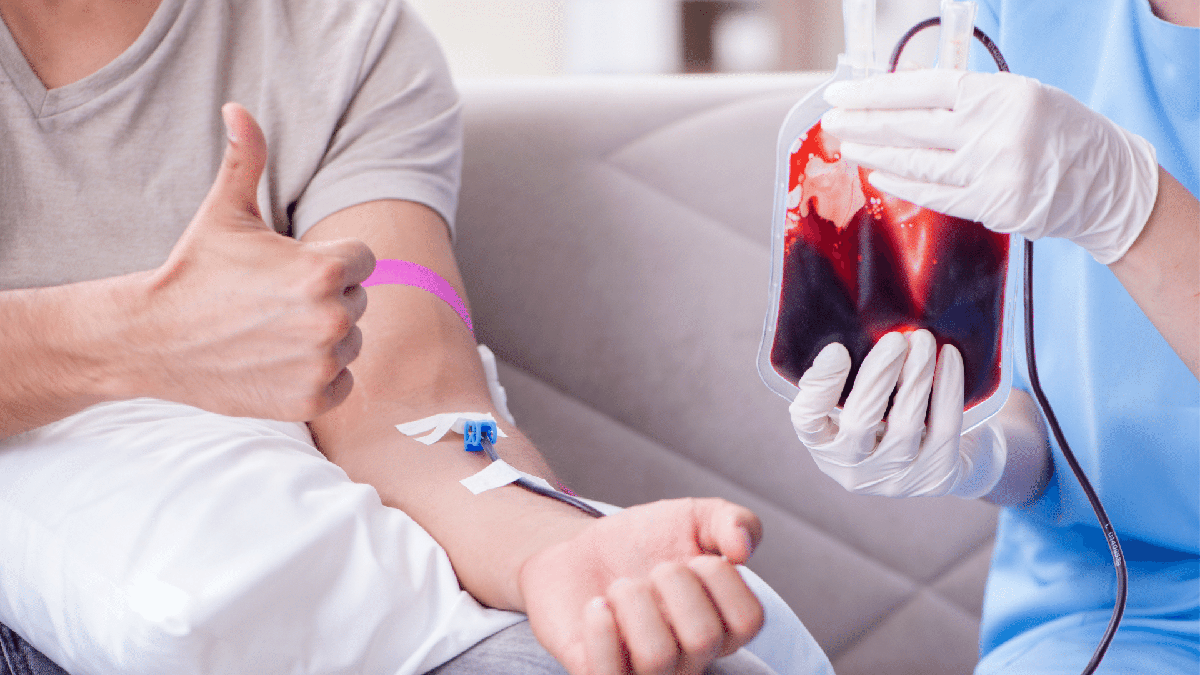 Homem faz sinal de positivo ao lado de bolsa de sangue após doação