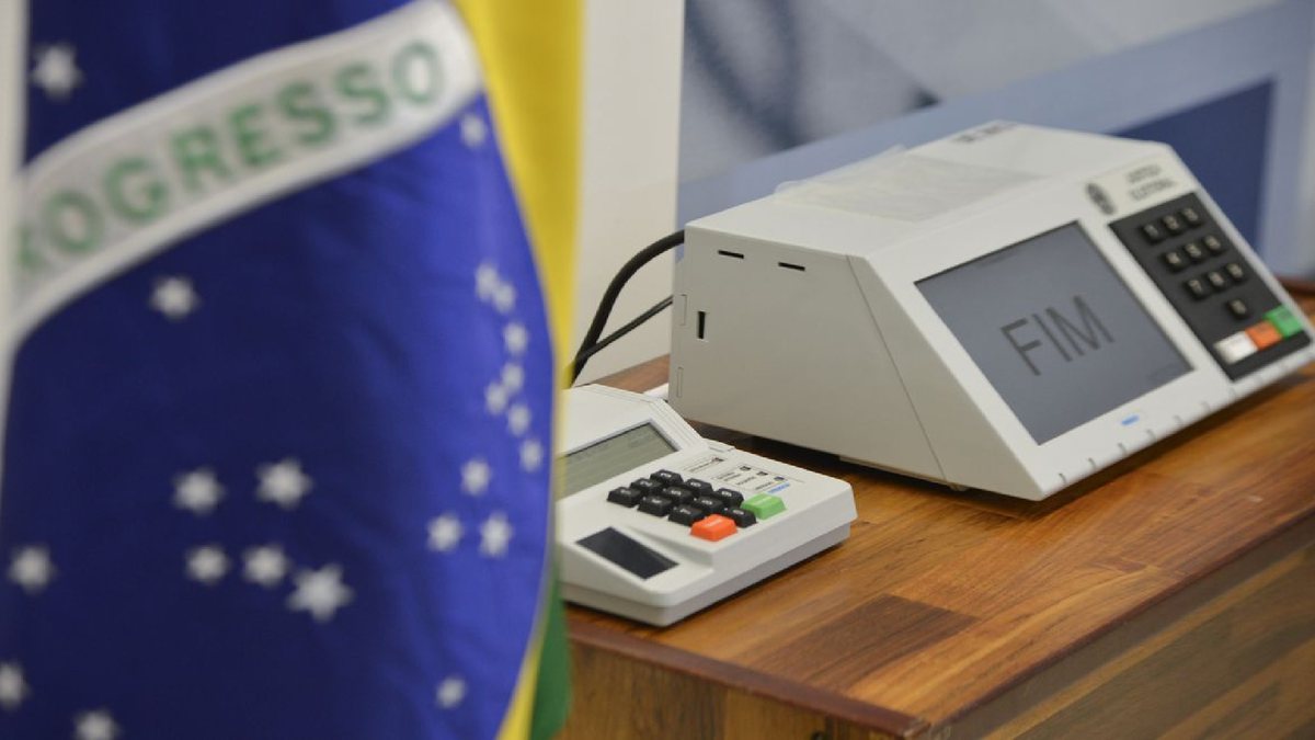 Uma urna eletrônica, do lado a bandeira do Brasil