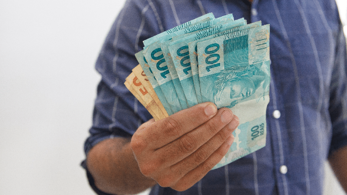 Homem segurando notas de R$ 100 e R$ 50