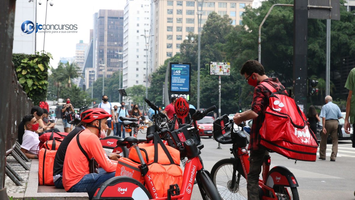 Trabalhadores por aplicativo com bicicletas e mochilas nas costas