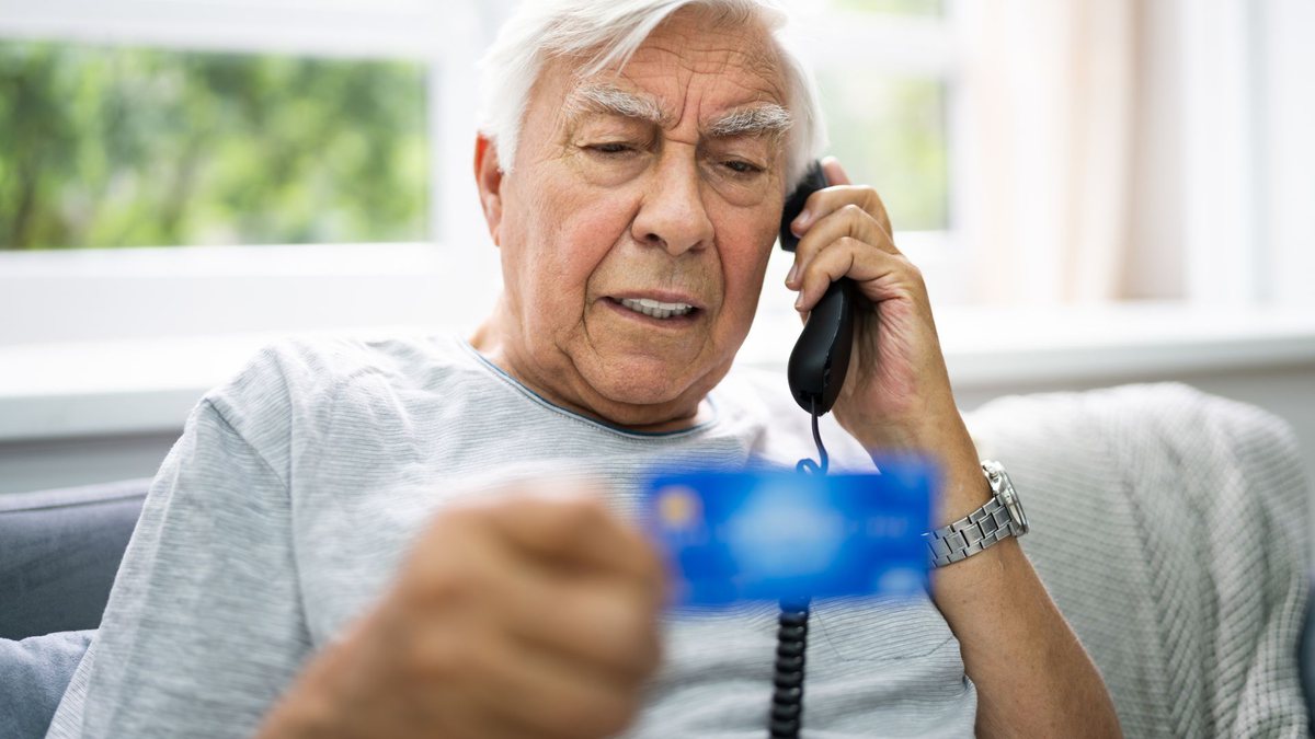 Imagem meramente ilustrativa, um idoso segura o cartão do banco e fala ao telefone