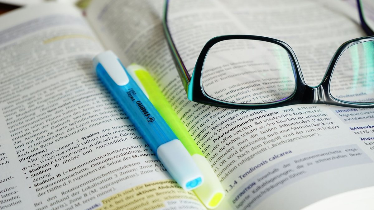 Óculos e caneta marca-texto em cima de livro