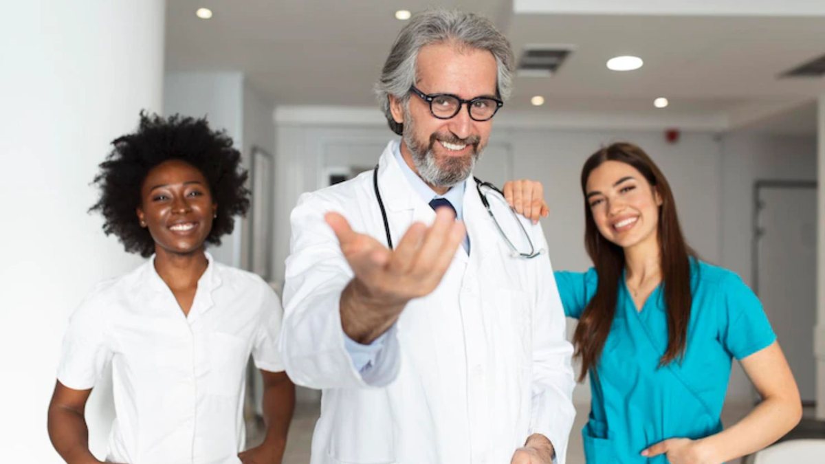 À esquerda: mulher negra, profissional de saúde. Ao centro: homem branco, grisalho, de jaleco e estetoscópio. À sua direita, uma mulher jovem de uniforme de hospital, azul. | Foto: Freepik