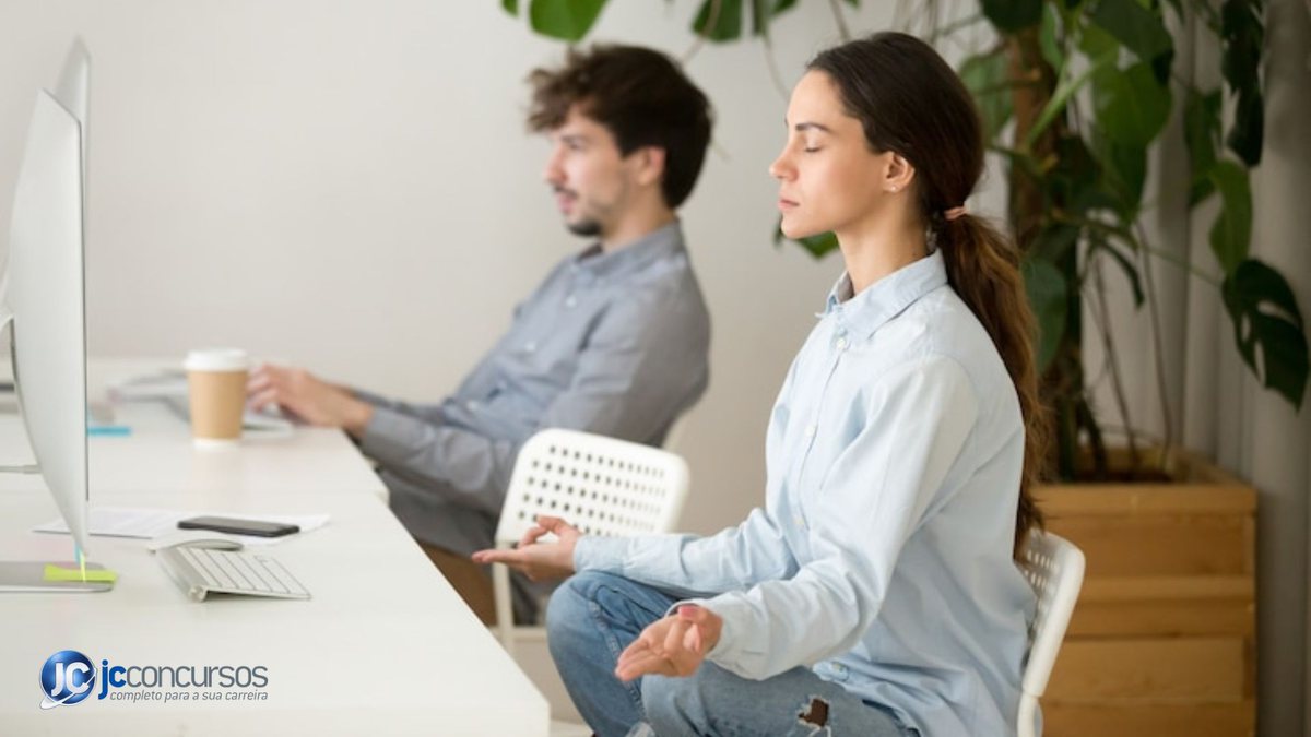 Mulher aplicando a técnica de meditação mindfulness em escritório, ao lado de um homem - Freepik