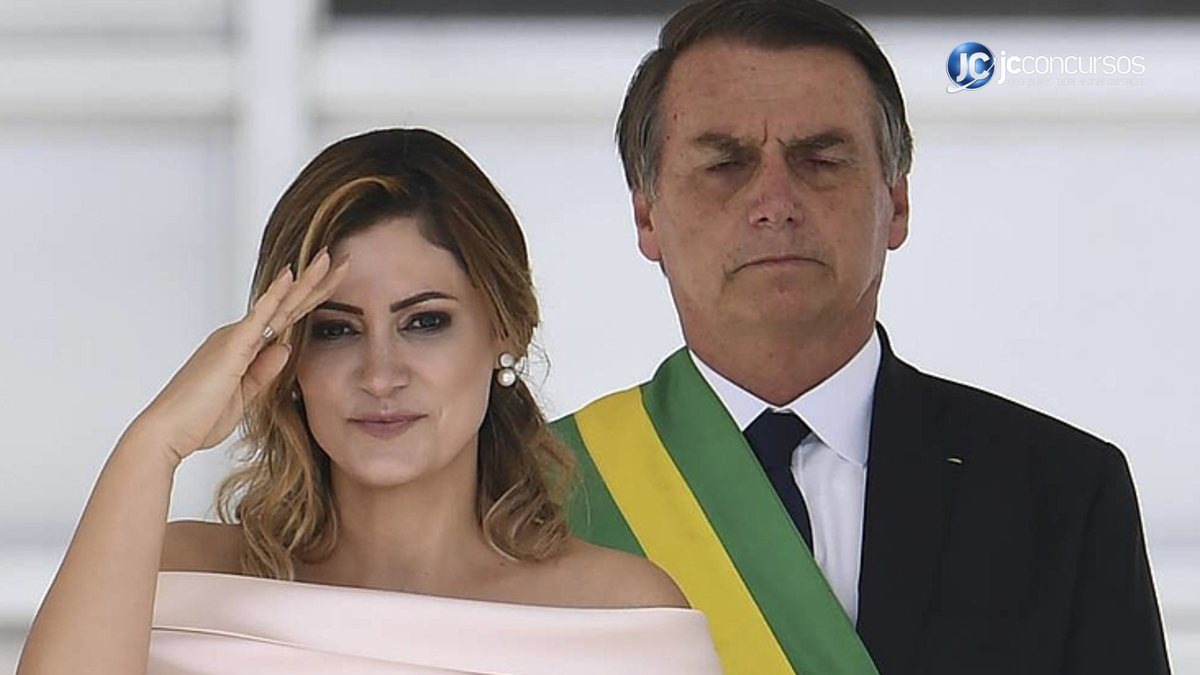 Jair Bolsonaro com faixa presidencial e Michele Bolsonaro ao seu lado com mão na cabeça
