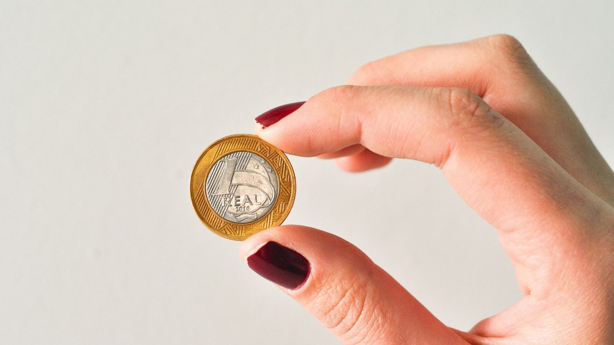 Uma mulher segura uma moeda de R$ 1 real