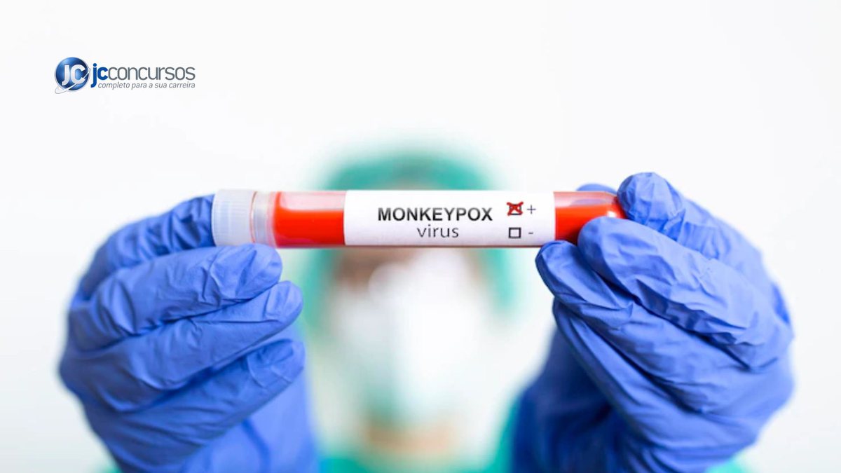 Mãos com luvas plásticas azuis segurando tubo com líquido vermelho dentro e adesivo escrito "Monkeypox" | Foto: Freepik
