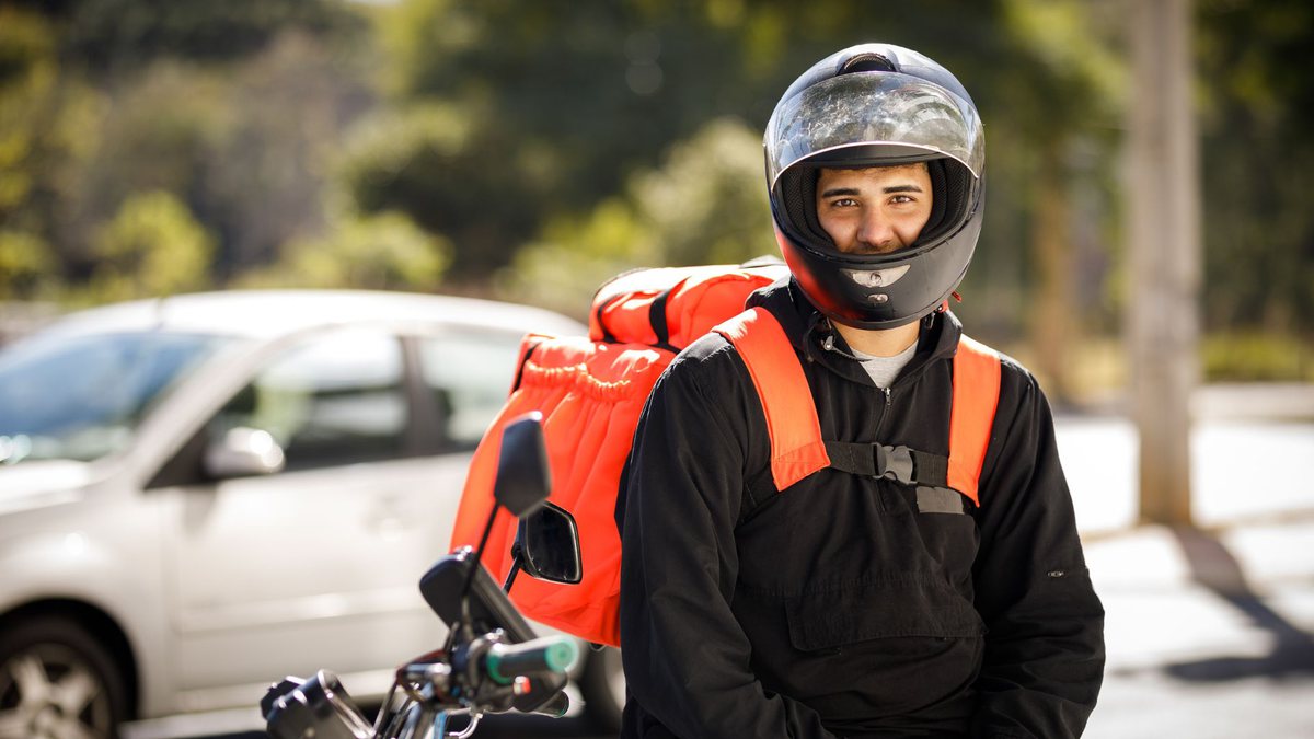 Motoboy com mochila laranha e capacete preto
