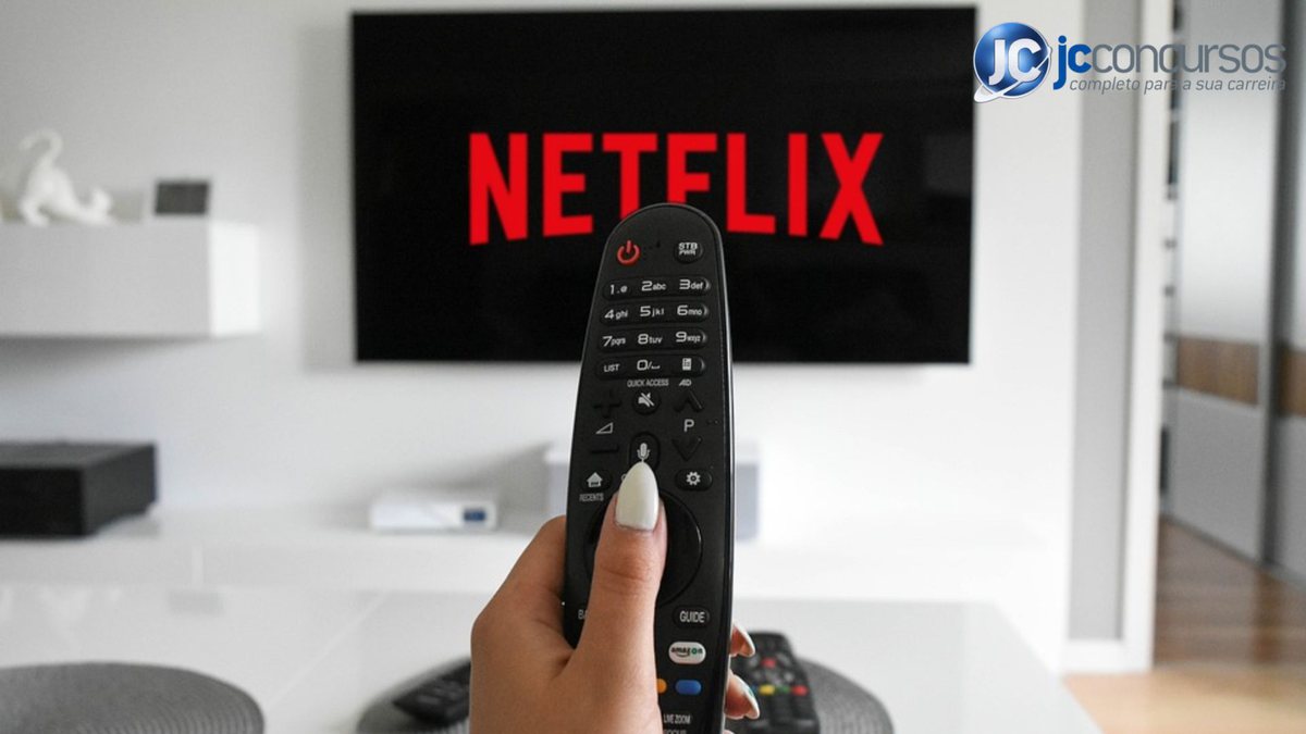 Mão segura controle remoto da TV, que mostra o nome Netflix na tela