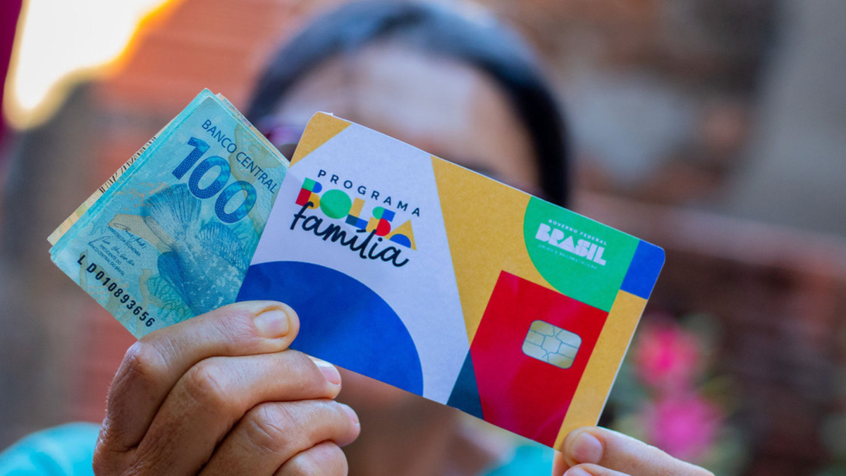 Mulher segura cartão do novo Bolsa Família e notas de cem reais