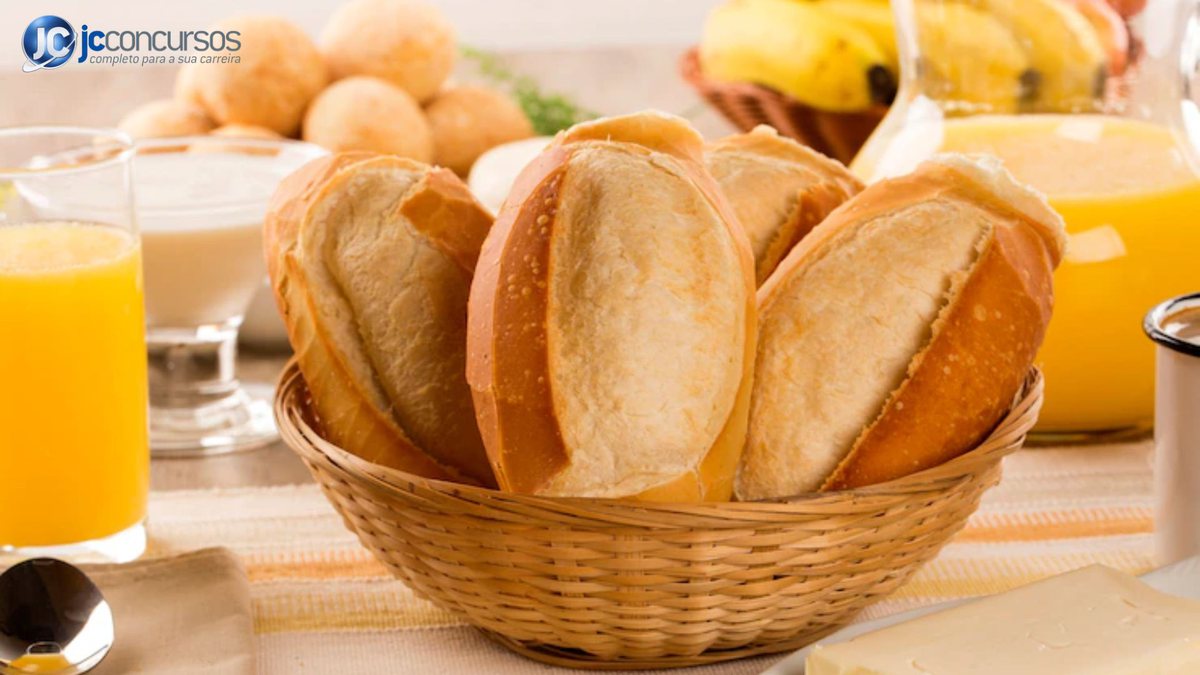 Cesta com pães franceses e outros alimentos ao redor, como sucos, queijos e bananas - Freepik