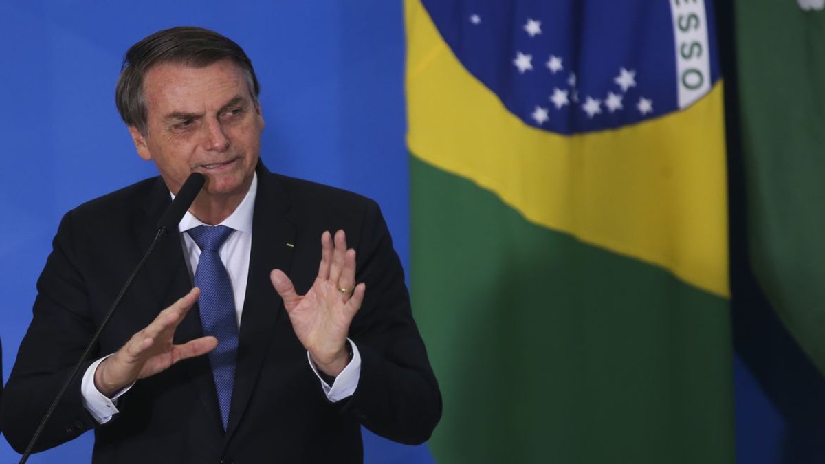 Bolsonaro fala em microfone com bandeira do Brasil ao fundo