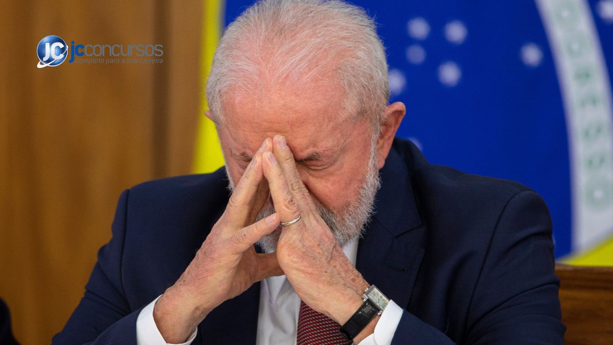 Lula com cabeça baixa e mãos no rosto, com bandeira do Brasil ao fundo - Divulgação
