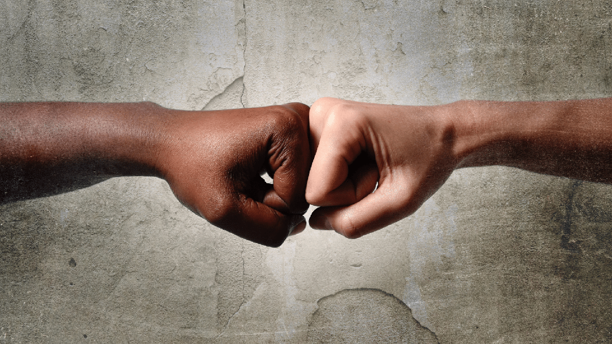 Pessoas branca e negra tocam as mãos com punho fechado