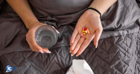 Mulher na cama com medicamentos na mão e copo d'água - Freepik